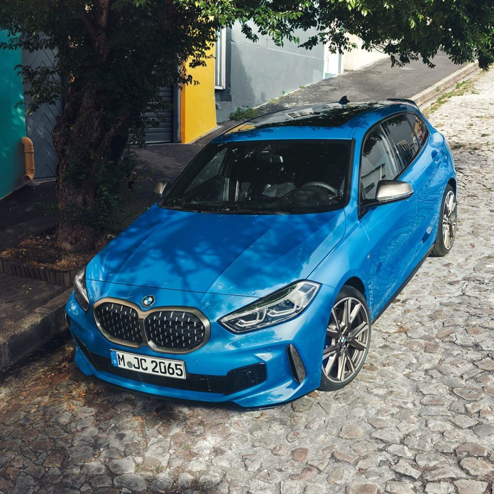 BMW radu 1 odstavené pri ceste. BMW radu 1 v metalickej farbe Misano Blue, trojštvrťový predný pohľad, parkovanie pri ceste z vtáčej perspektívy.