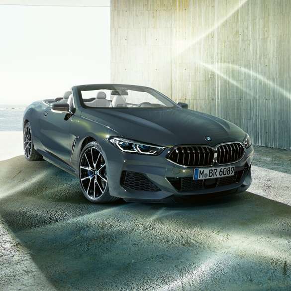 BMW M850i xDrive Cabrio, trojštvrťový predný pohľad. BMW M850i xDrive Cabrio v metalickej farbe Dravit Grey s otvorenou strechou, trojštvrťový predný pohľad, vozidlo stojace na pobreží.