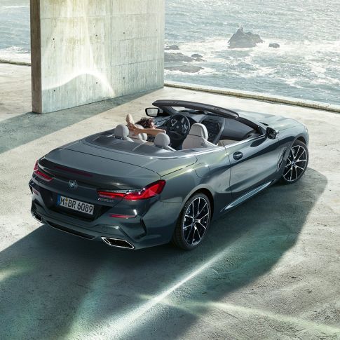 BMW M850i xDrive Cabrio, pohľad z vtáčej perspektívy. BMW M850i xDrive Cabrio v metalickej farbe Dravit Grey s otvorenou strechou, pohľad z vtáčej perspektívy, vozidlo odparkované v betónovej budove na brehu oceánu.