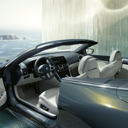 BMW M850i xDrive Cabrio, interiér. BMW M850i xDrive Cabrio v metalickej farbe Dravit Grey s otvorenou strechou, interiér s M koženým volantom a koženým čalúnením BMW Individual Merino Ivory White.