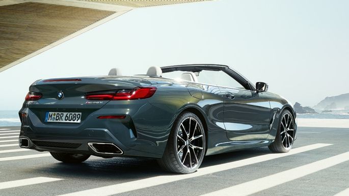 BMW M850i xDrive Cabrio, trojštvrťový zadný pohľad. BMW M850i xDrive Cabrio v metalickej farbe Dravit Grey s otvorenou strechou, trojštvrťový zadný pohľad, stojace vozidlo s výhľadom na oceán.