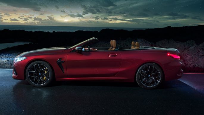BMW M8 Competition Cabrio, bočný pohľad. BMW M8 Competition Cabrio v metalickej farbe Motegi Red s otvorenou strechou, bočný pohľad, vozidlo stojace v noci pod hviezdnou oblohou.