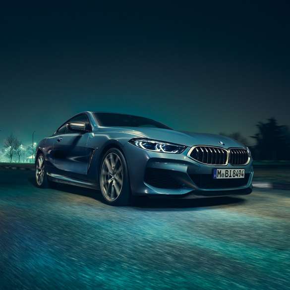 BMW M850i xDrive Coupé, trojštvrťový predný pohľad z ľavej strany. BMW M850i xDrive Coupé v metalickej farbe Barcelona Blue, trojštvrťový predný pohľad na jazdiace vozidlo v noci z ľavej strany.