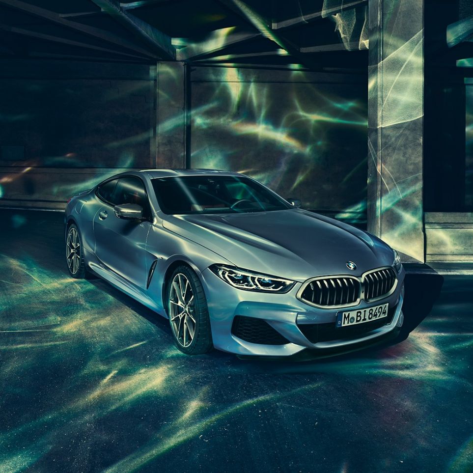 BMW M850i xDrive Coupé, trojštvrťový predný pohľad z ľavej strany. BMW M850i xDrive Coupé v metalickej farbe Barcelona Blue, trojštvrťový predný pohľad z ľavej strany na vozidlo stojace pred priečelím budovy.