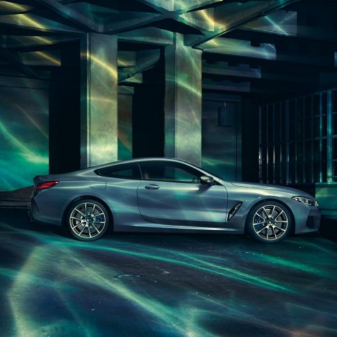 BMW M850i xDrive Coupé, bočný pohľad. BMW M850i xDrive Coupé v metalickej farbe Barcelona Blue, bočný pohľad na stojace vozidlo pred priečelím budovy.