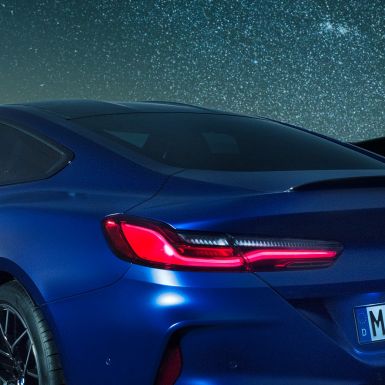 M zadný spojler BMW M8 Competition Coupé v metalickej farbe Marina Bay Blue, nočný detailný pohľad na ramennú časť s M zadným spojlerom v karbónovej úprave.