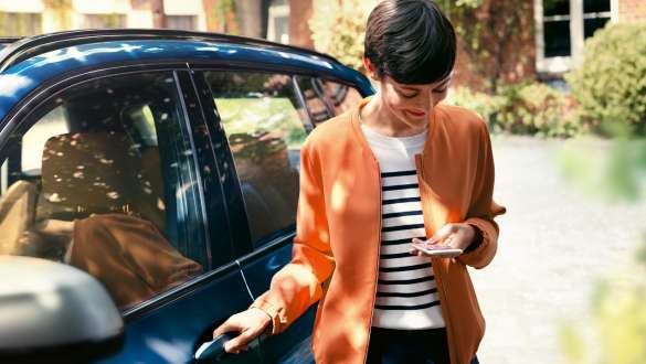Žena sa pozerá na svoj smartfón a otvára dvere svojho BMW BMW Teleservices žena sa pozerá na svoj smartfón a otvára dvere svojho BMW