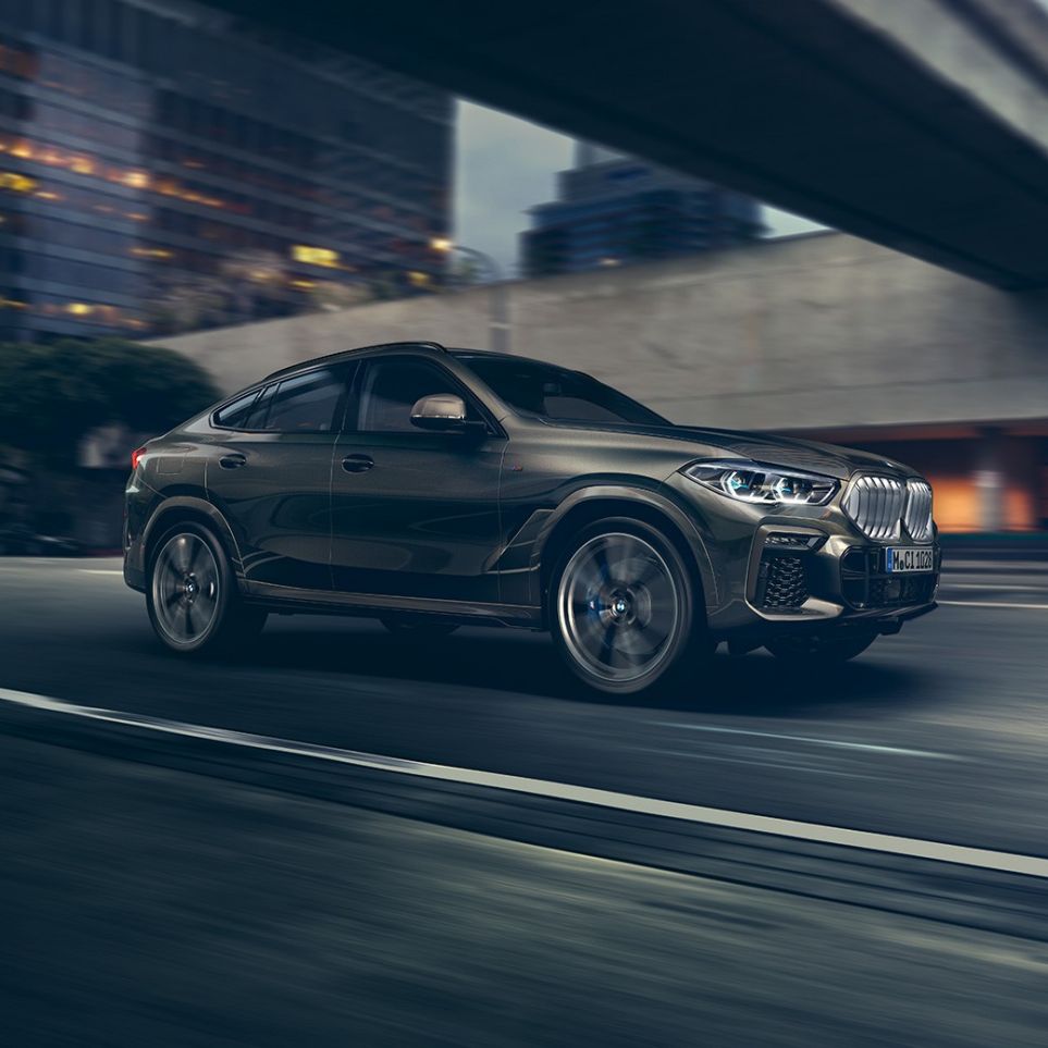 BMW X6 jazda. BMW X6, trojštvrťový predný pohľad na jazdiace vozidlo pred kulisami mesta.