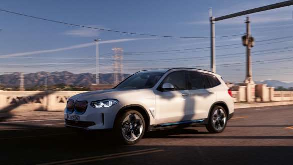 Adaptívny podvozok BMW iX3 G08 2020 jazda na ulici Adaptívny M podvozok BMW iX3 G08 2020 metalíza Mineral White predobočný pohľad jazda na ulici