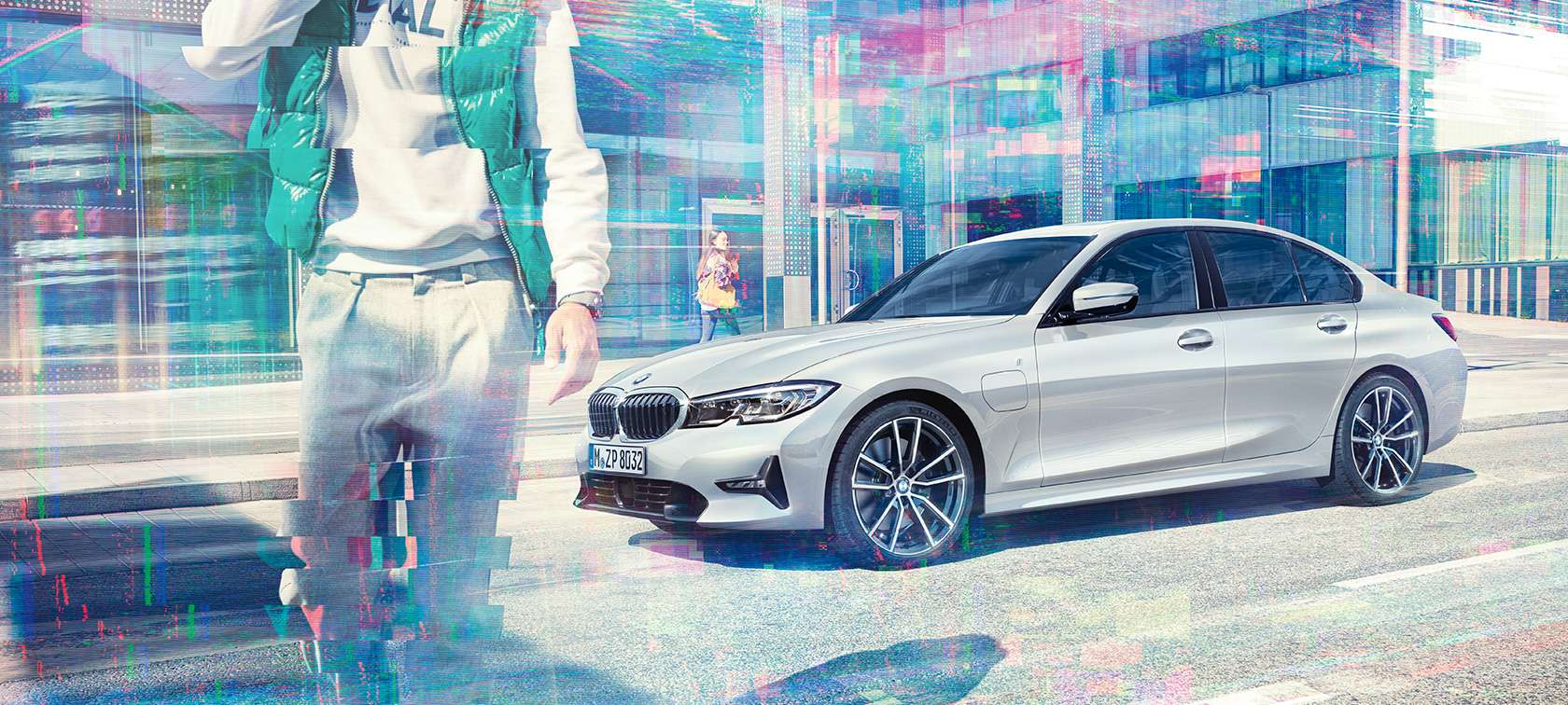 BMW radu 3 Sedan, bočný záber na BMW 330e. Bočný záber na BMW 330e Sedan stojace pred sklenenou mestskou budovou s chodcami v pohybe.