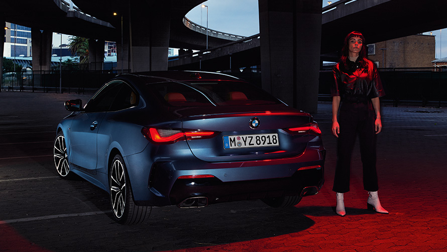 BMW radu 4 Coupé (G22) metalíza Arctic Race Blue, zadný pohľad s osobou BMW radu 4 Coupé (G22) metalíza Arctic Race Blue, zadný pohľad s osobou