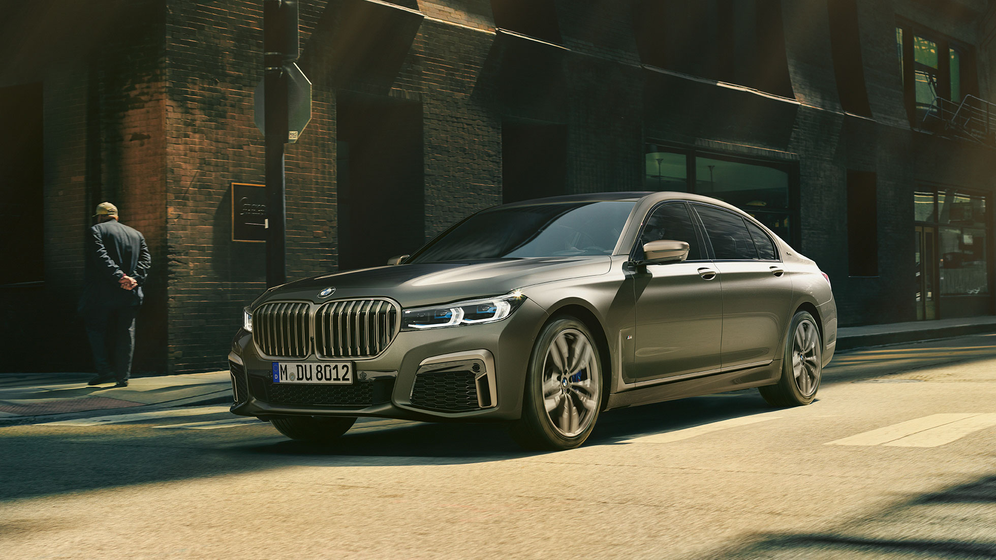 BMW M760Li xDrive pred kulisami mesta BMW M760Li xDrive v bočnom prednom pohľade jazdiace po ulici pred kulisami mesta