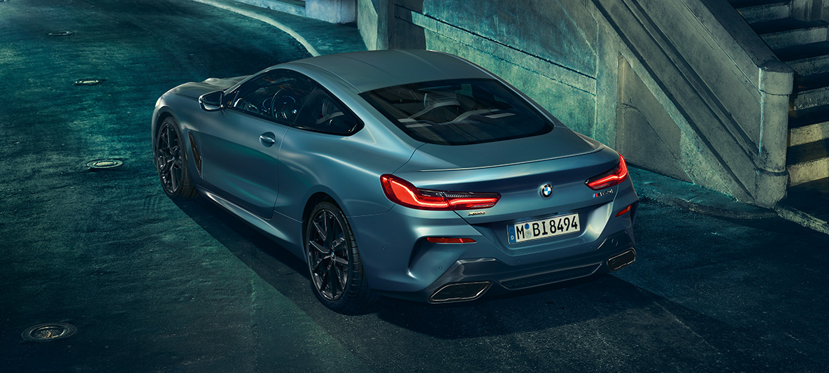 BMW M850i Coupé First Edition, trojštvrťový pohľad zozadu Trojštvrťový zadný pohľad na stojace BMW M850i Coupé First Edition pred kulisami mesta.