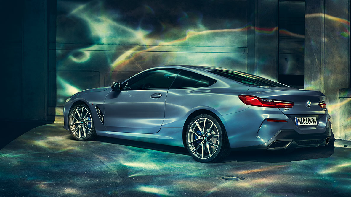 Zadobočný záber BMW radu 8 Coupé. Zadobočný záber BMW radu 8 Coupé v noci s kulisou mesta v pozadí.