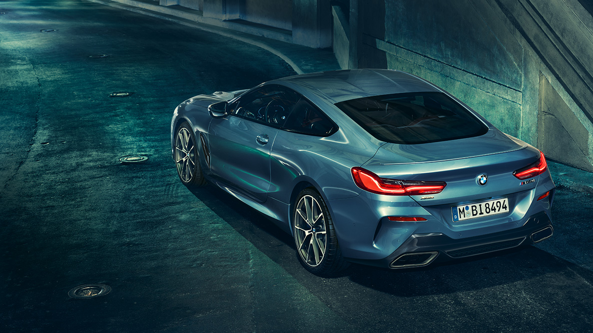 BMW radu 8 Coupé, zadobočný záber. Zadobočný záber BMW radu 8 Coupé pred kulisou nočného mesta.