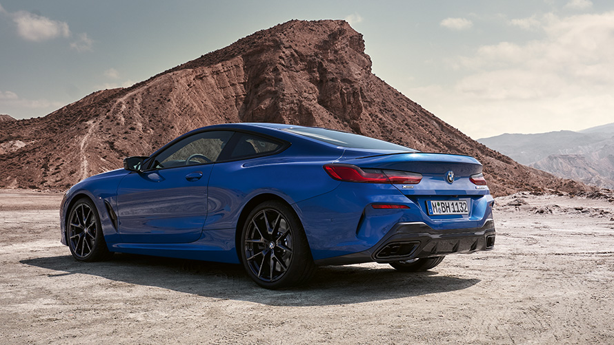 Zadobočný pohľad BMW radu 8 Coupé M Sport balík G15 LCI Facelift 2022 BMW radu 8 Coupé M Sport balík G15 LCI Facelift 2022 metalíza M Portimao Blue zadobočný pohľad statický pred kameňmi