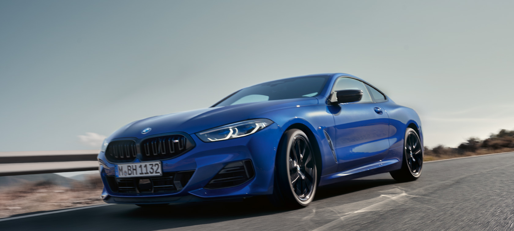 BMW radu 8 Coupé G15 LCI Facelift 2022 BMW M850i xDrive metalíza M Portimao Blue predný záber zdola BMW radu 8 Coupé G15 LCI Facelift 2022 BMW M850i xDrive metalíza M Portimao Blue predný záber zdola jazda na vidieckej ceste s kopcami v pozadí