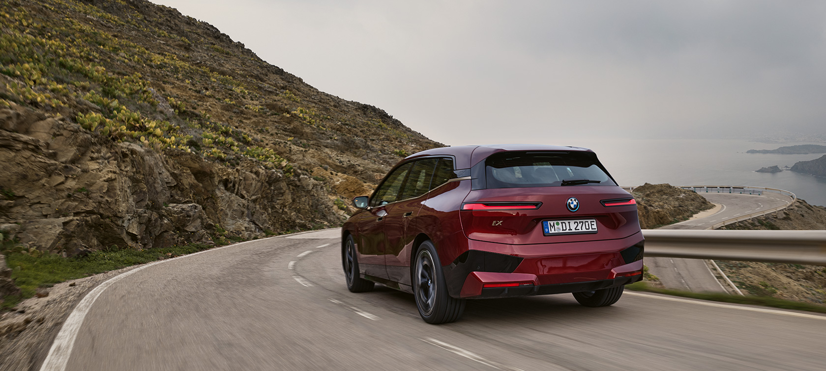 BMW iX i20 2021 elektrické SUV BMW iX xDrive50 jazda na pobrežnej ceste BMW iX i20 2021 elektrické SUV BMW iX xDrive50 Aventurine Red zadný pohľad jazda na pobrežnej ceste