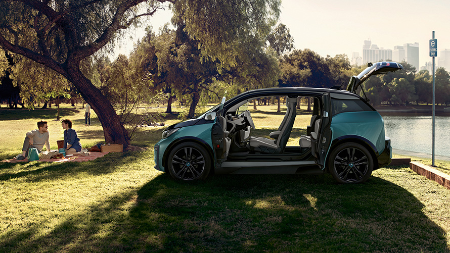 BMW i3 2018 v parku BMW i3 I01 2018 Jucaro Beige so zvýraznením v metalíze Frozen Grey bočný pohľad s otvorenými dverami v parku