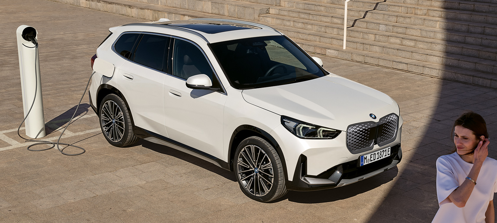 BMW iX1 U11 BEV bočný pohľad BMW iX1 U11 BEV 2022 metalíza Mineral White bočný pohľad nabíjanie pri schodoch