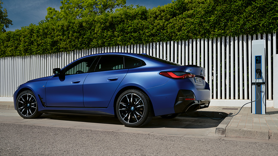 Bočný pohľad BMW i4 M50 G26 2021 na verejnej rýchlonabíjacej stanici BMW i4 M50 G26 2021 BMW Individual metalíza Frozen Portimao Blue bočný pohľad na verejnej rýchlonabíjacej stanici