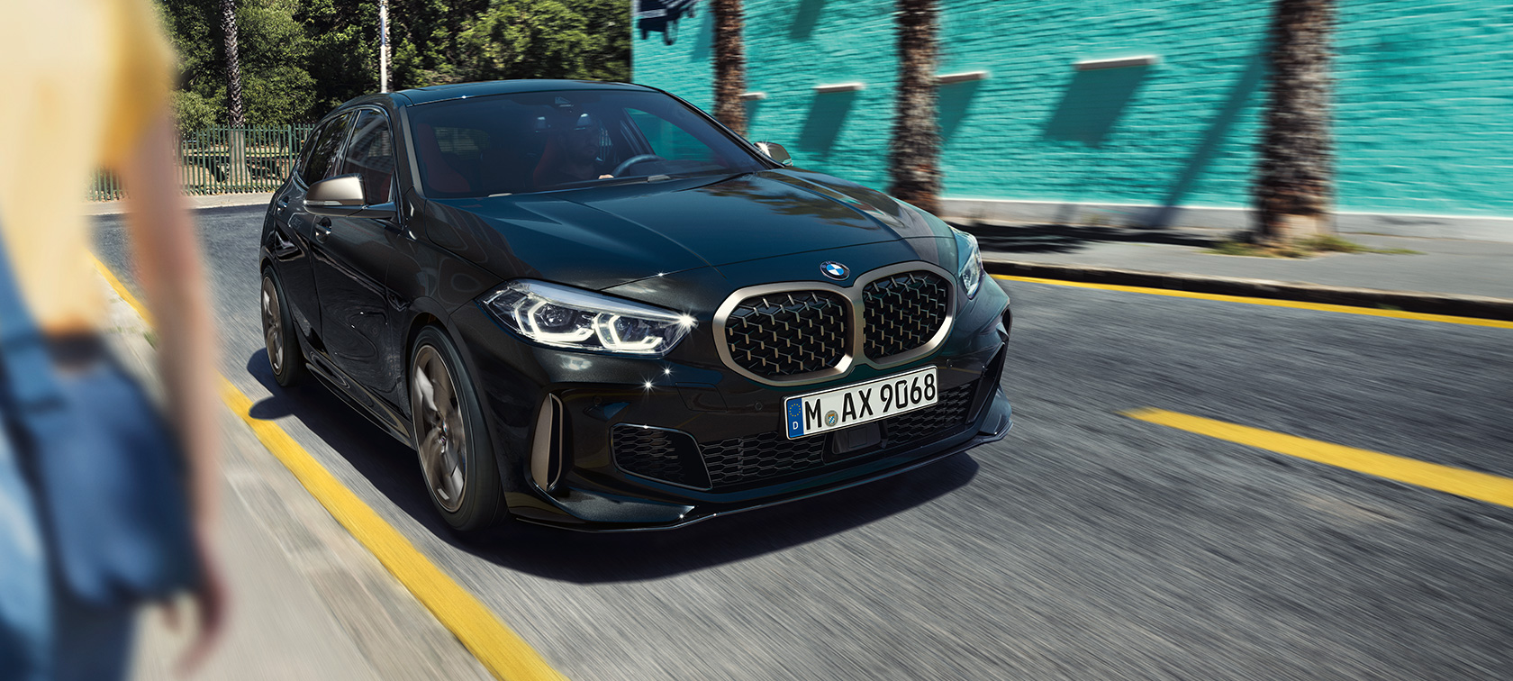 BMW M135i xDrive, trojštvrťový predný pohľad. BMW M135i xDrive v metalickej farbe Black Sapphire, trojštvrťový predný pohľad počas jazdy.