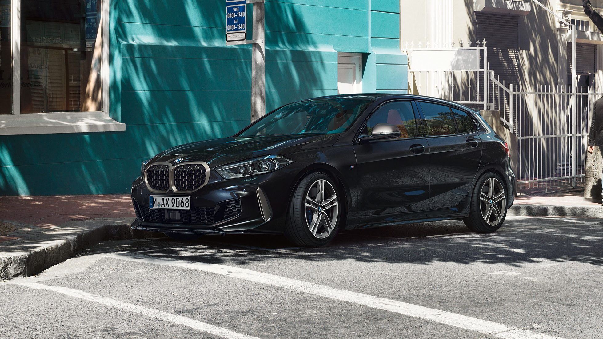BMW M135i xDrive, trojštvrťový bočný pohľad. Úplne nové BMW M135i xDrive v metalickej farbe Black Sapphire, trojštvrťový bočný pohľad na odparkované vozidlo.