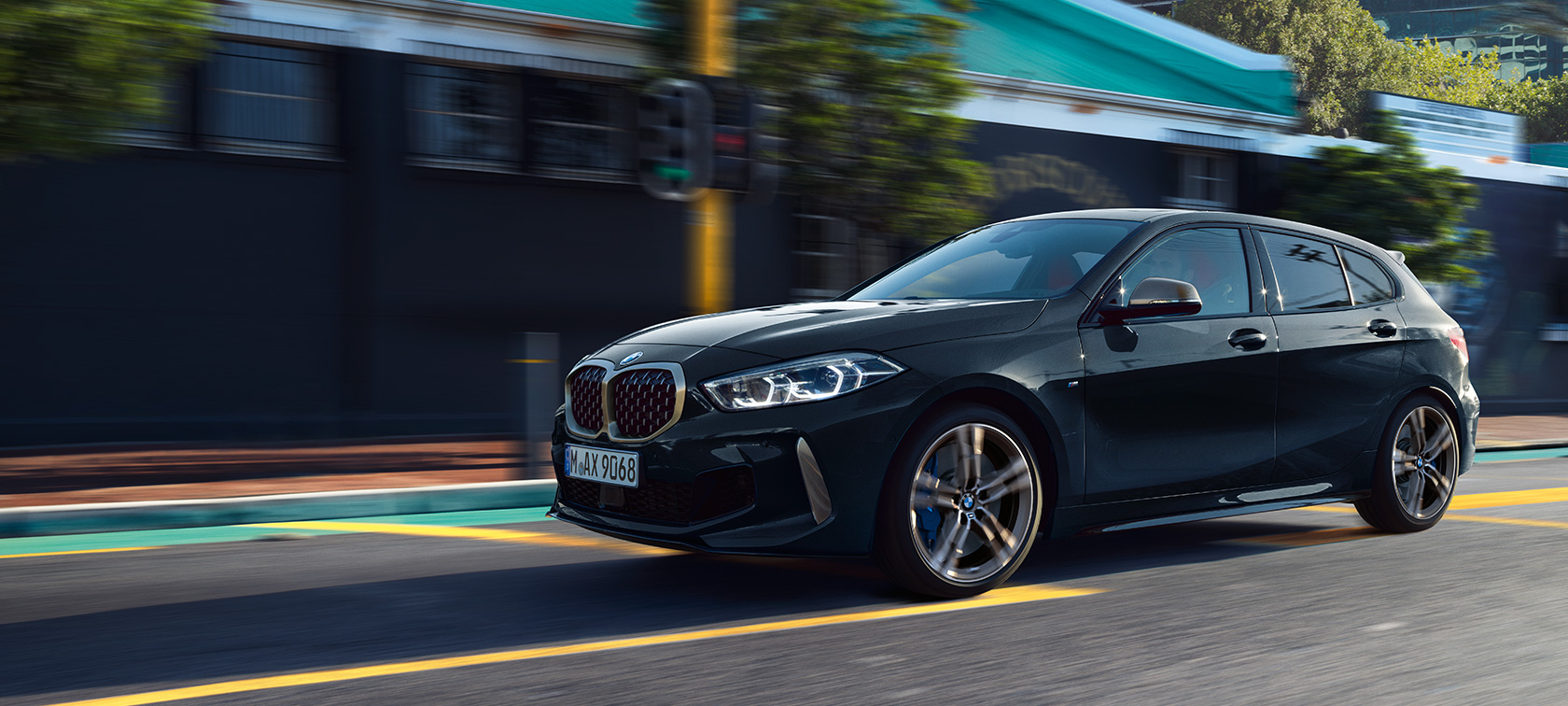 Úplne nové BMW M135i xDrive Úplne nové BMW M135i xDrive v metalickej farbe Black Sapphire, trojštvrťový bočný pohľad na vozidlo počas jazdy.