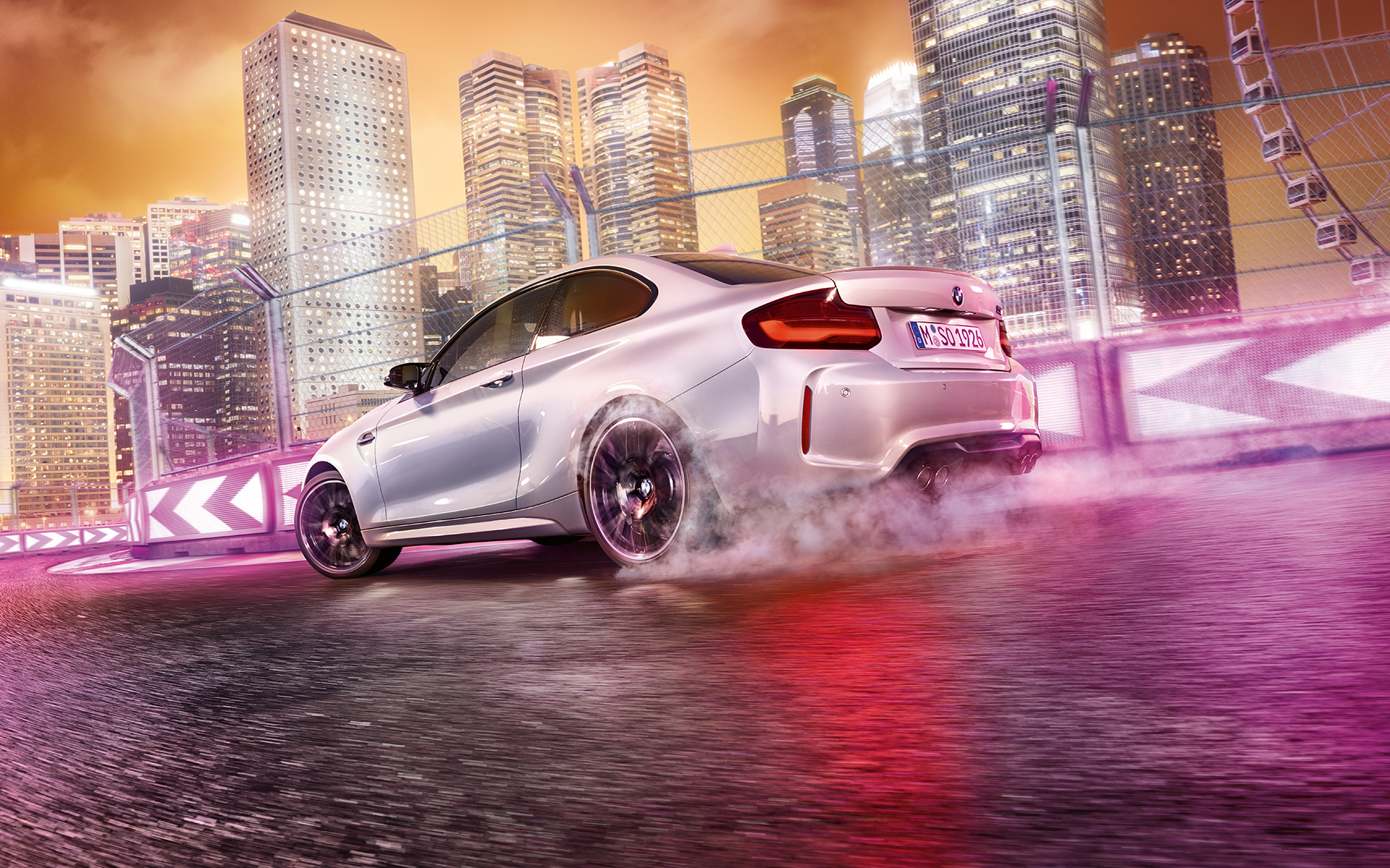 BMW M2 Competition pridáva plyn Biele BMW M2 Competition driftuje na pretekárskej trati pred kulisou nočného mesta.