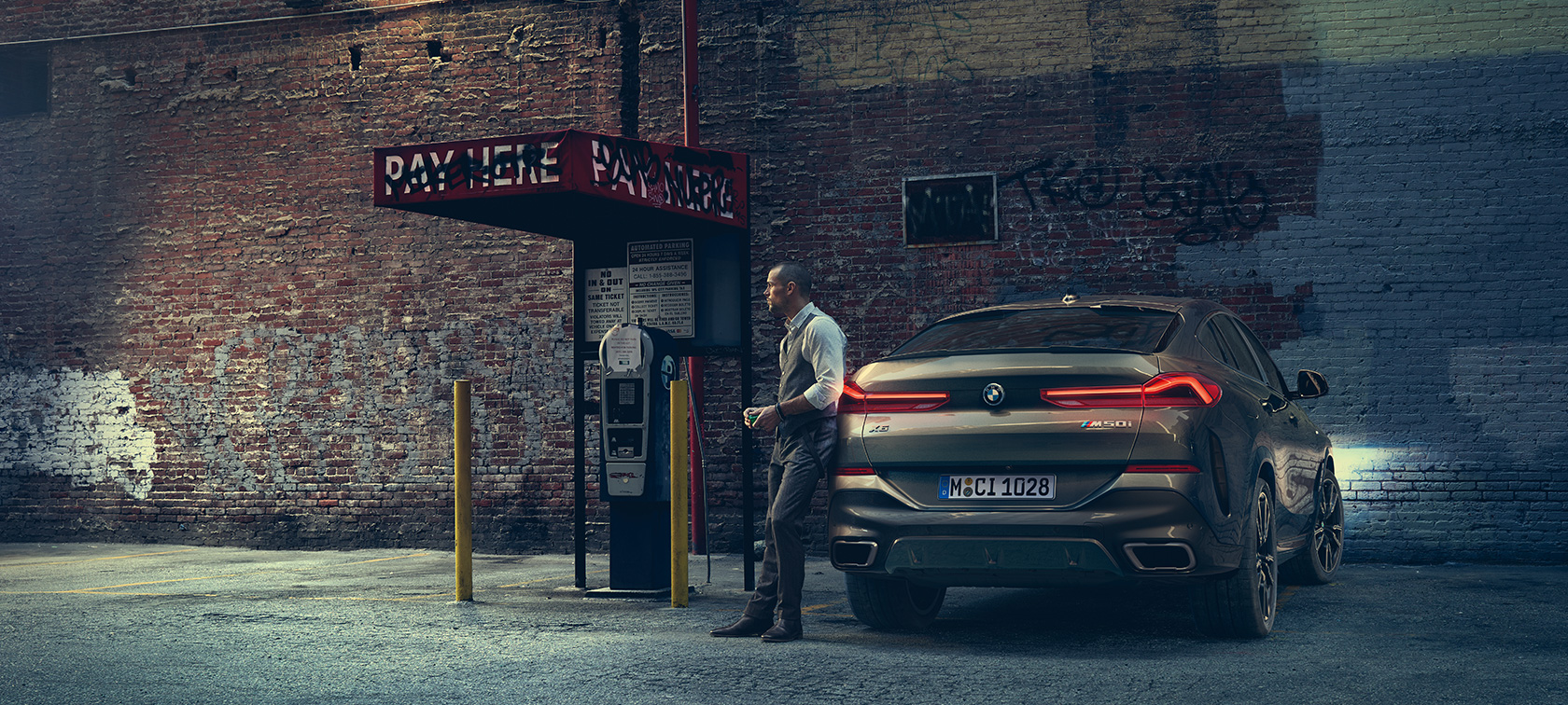 Zadná časť BMW X6 M50i. Muž opierajúci sa o zadnú časť BMW X6 M50i.