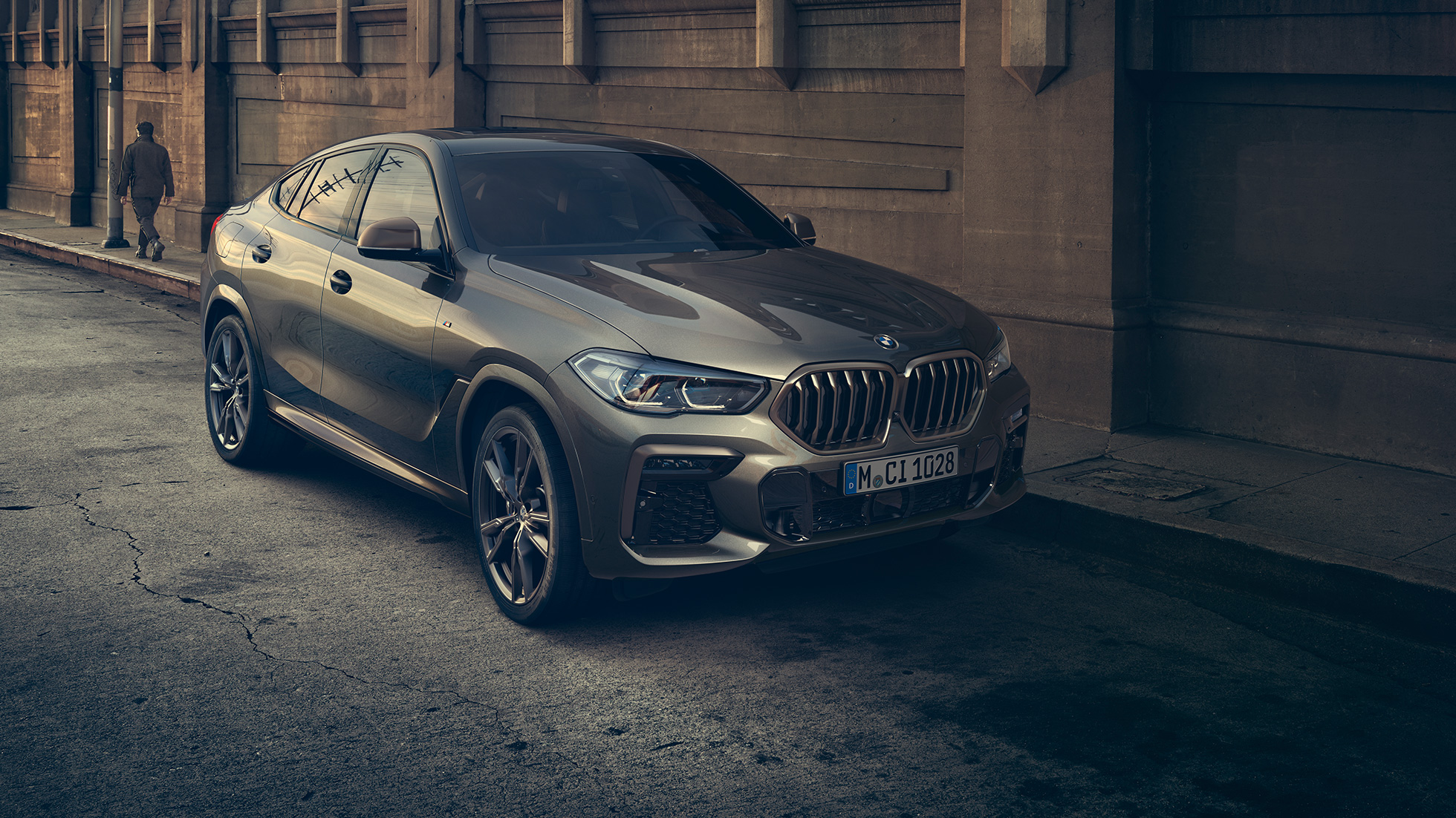 BMW X6 M50i stojace. BMW X6 M50i, trojštvrťový predný pohľad na vozidlo stojace pred kulisami mesta.