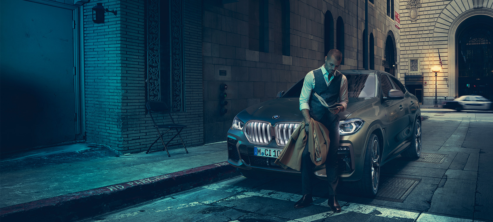 Predná časť BMW X6 M50i. Muž opierajúci sa o prednú časť BMW X6 M50i.