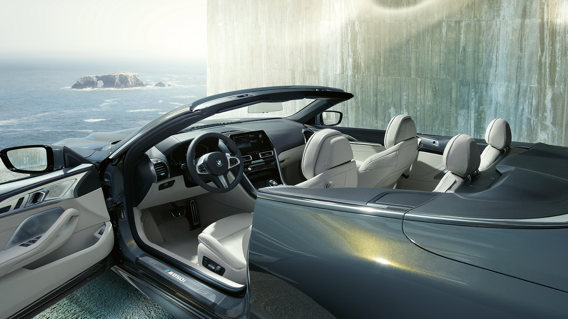 BMW M850i xDrive Cabrio, interiér. BMW M850i xDrive Cabrio v metalickej farbe Dravit Grey s otvorenou strechou, interiér s M koženým volantom a koženým čalúnením BMW Individual Merino Ivory White.