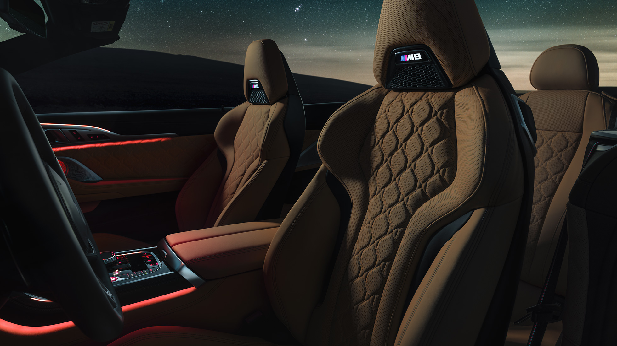 M Sport sedadlá čalúnené kožou Merino. BMW M8 Competition Cabrio s otvorenou strechou pod hviezdnou oblohou, interiér s M Sport sedadlami čalúnenými kožou Merino a červeným ambientným osvetlením.