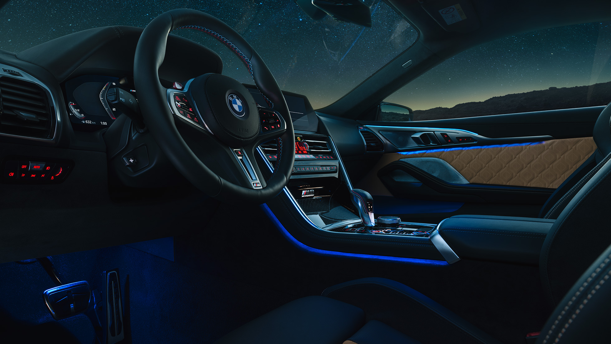 BMW M8 Competition Coupé, kokpit. BMW M8 Competition Coupé, kokpit v noci s M koženým volantom a modrým ambientným svetlom.