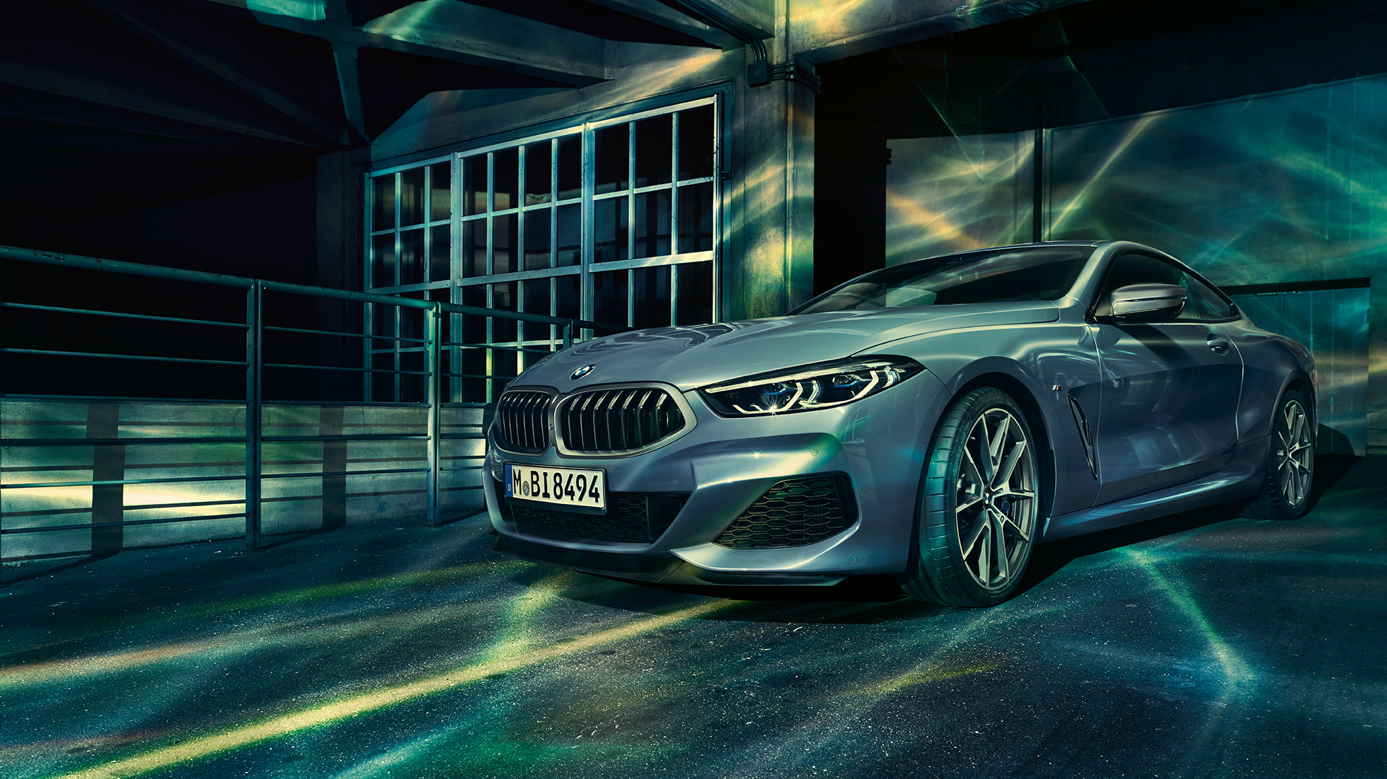 BMW M850i xDrive Coupé, trojštvrťový predný pohľad. BMW M850i xDrive Coupé v metalickej farbe Barcelona Blue, trojštvrťový predný pohľad pred priečelím budovy.