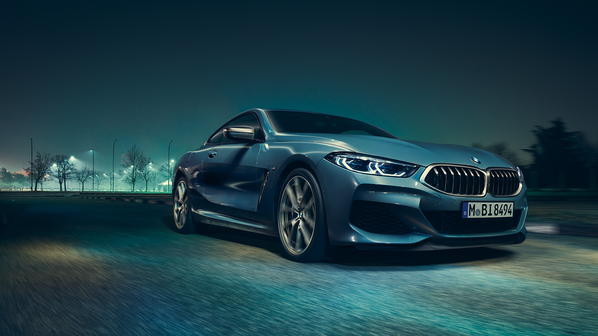 BMW M850i xDrive Coupé, trojštvrťový predný pohľad z ľavej strany. BMW M850i xDrive Coupé v metalickej farbe Barcelona Blue, trojštvrťový predný pohľad na jazdiace vozidlo v noci z ľavej strany.