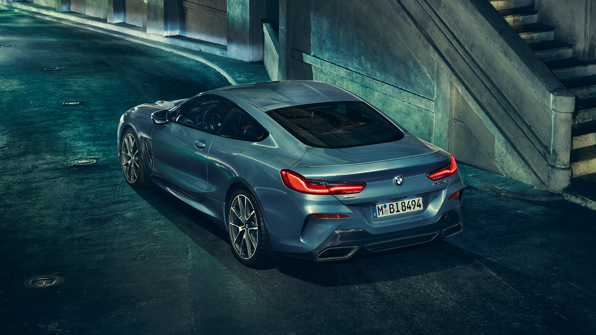 BMW M850i xDrive Coupé, trojštvrťový zadný pohľad z ľavej strany. BMW M850i xDrive Coupé v metalickej farbe Barcelona Blue, trojštvrťový zadný pohľad z ľavej strany na stojace vozidlo v noci.