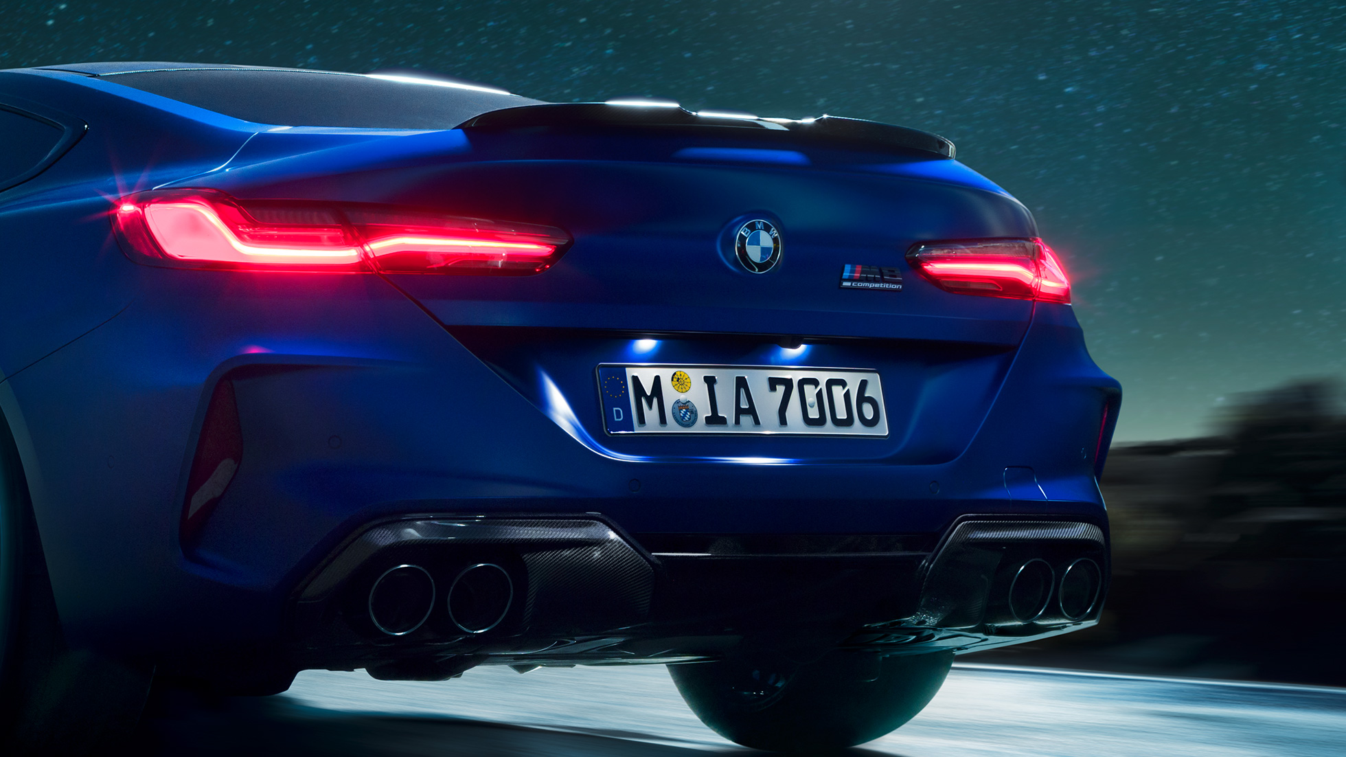M difúzor v čiernej karbónovej úprave. BMW M8 Competition Coupé v metalickej farbe Marina Bay Blue, detailný zadný pohľad v noci s M difúzorom v čiernej karbónovej úprave.