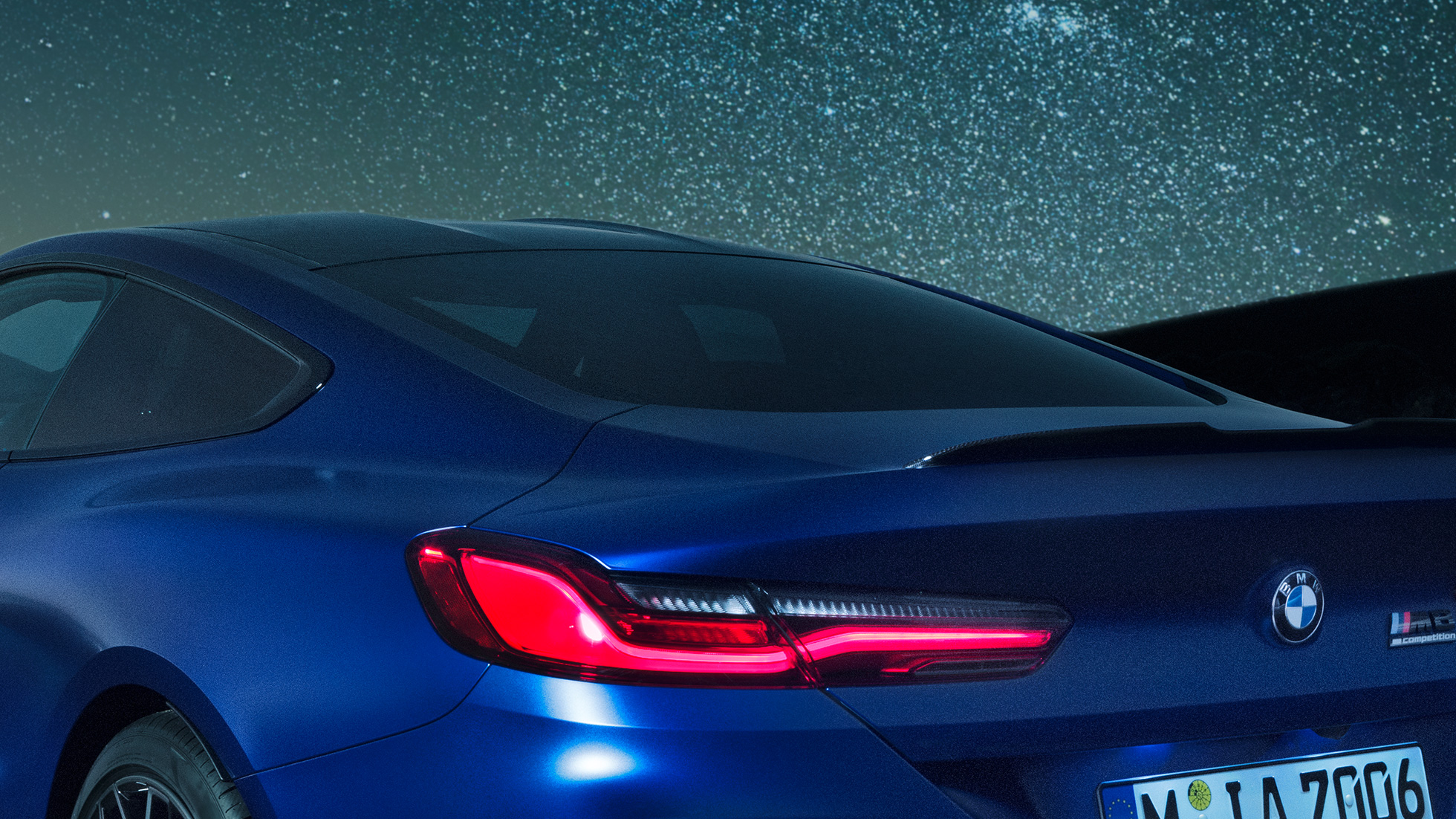 M zadný spojler BMW M8 Competition Coupé v metalickej farbe Marina Bay Blue, nočný detailný pohľad na ramennú časť s M zadným spojlerom v karbónovej úprave.