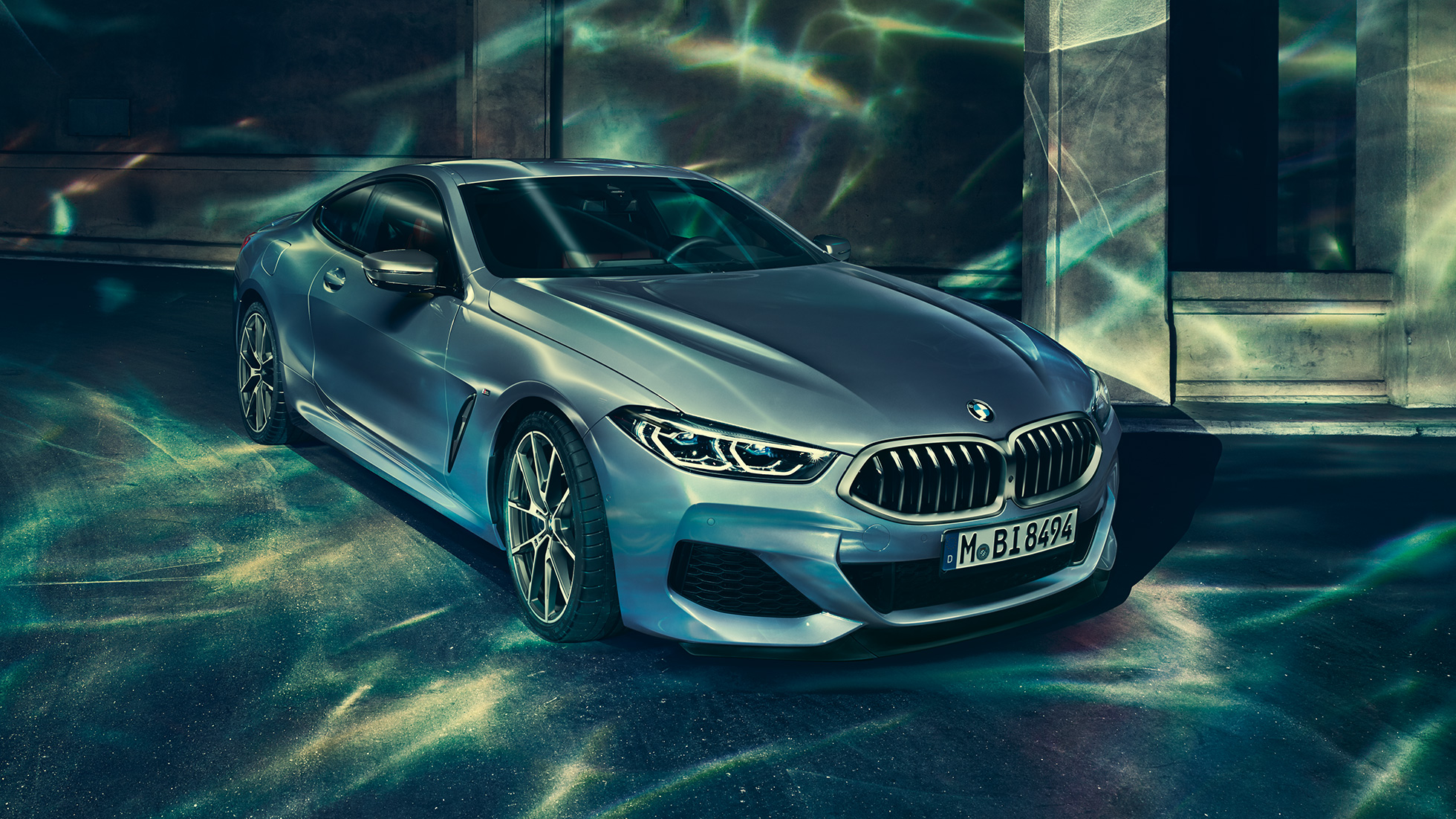 BMW M850i xDrive Coupé, trojštvrťový predný pohľad z ľavej strany. BMW M850i xDrive Coupé v metalickej farbe Barcelona Blue, trojštvrťový predný pohľad z ľavej strany na vozidlo stojace pred priečelím budovy.