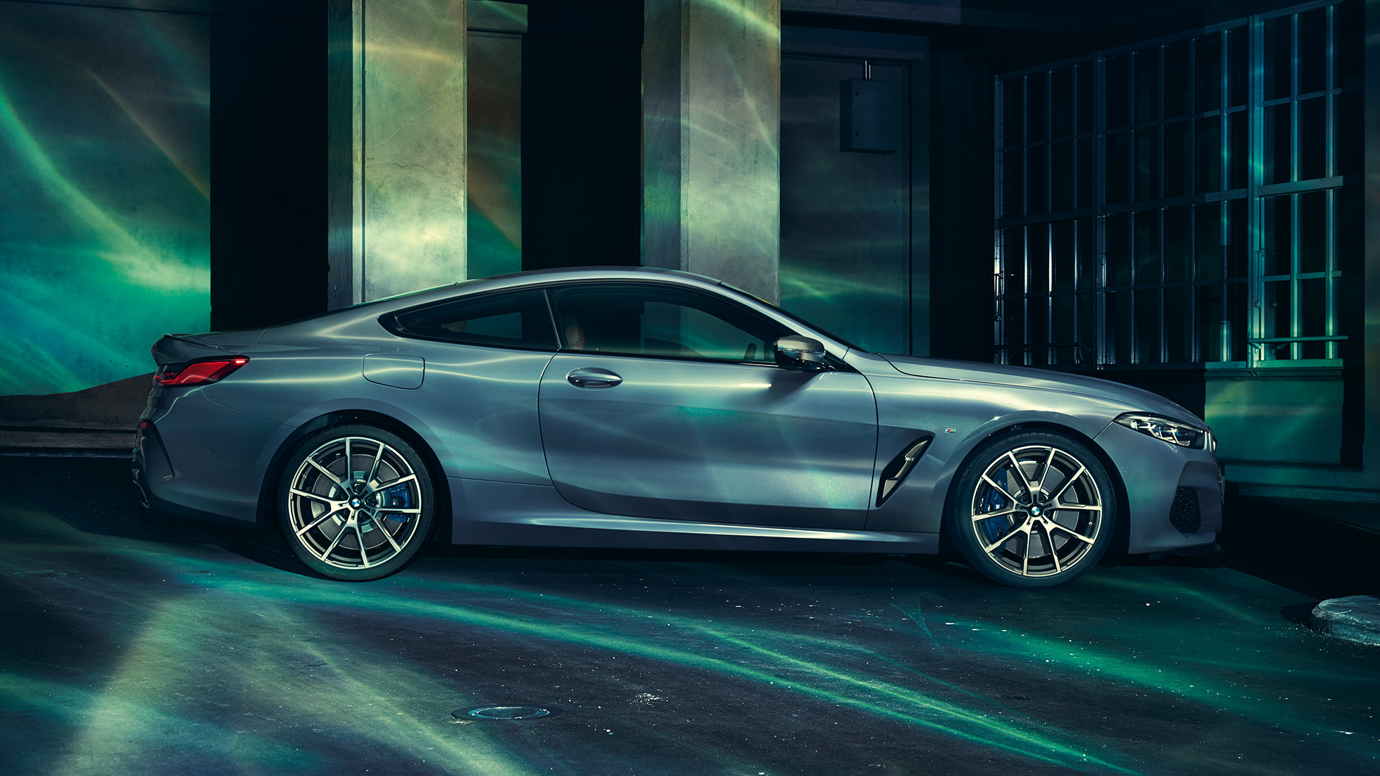 BMW M850i xDrive Coupé, bočný pohľad. BMW M850i xDrive Coupé v metalickej farbe Barcelona Blue, bočný pohľad na stojace vozidlo pred priečelím budovy.