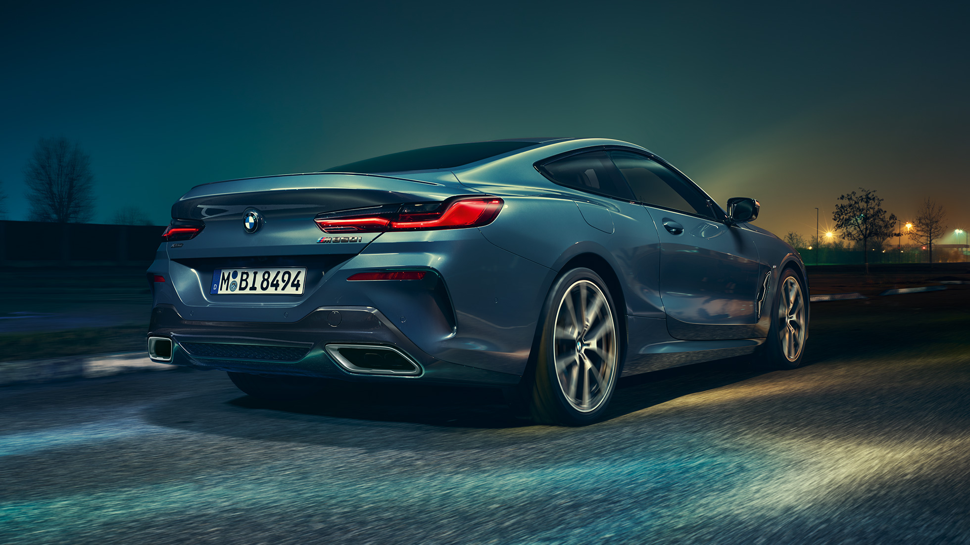 BMW M850i xDrive Coupé, zadný pohľad. BMW M850i xDrive Coupé v metalickej farbe Barcelona Blue, zadný pohľad na vozidlo jazdiace v noci.