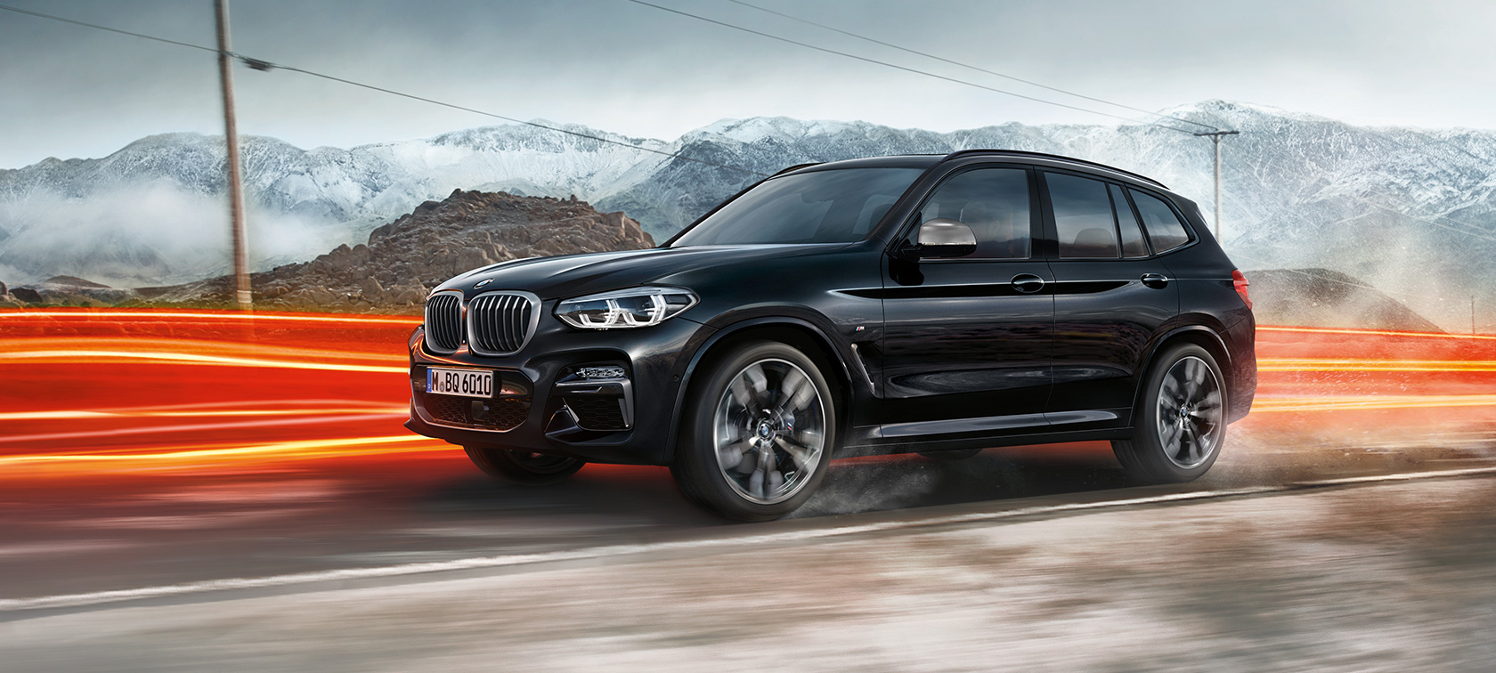 BMW X3 M40i a BMW X3 M40d, bočný pohľad. BMW X3 M40i a BMW X3 M40d v metalickej farbe Black Sapphire, jazda, exteriér, bočný pohľad pred horskou scenériou so svetelnými pásmi.