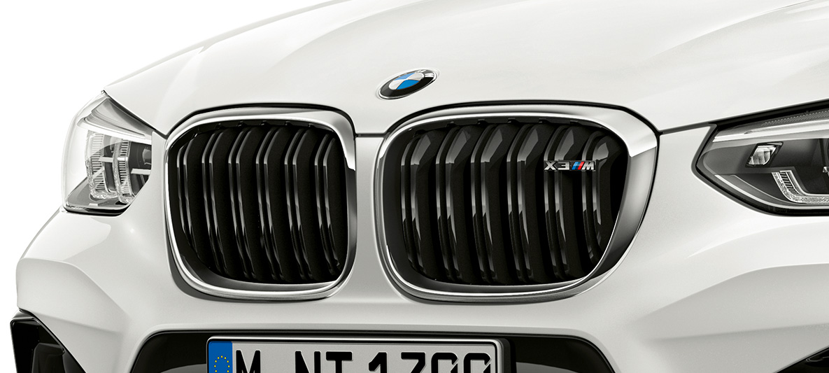 BMW X3 M, M mriežka chladiča. BMW X3 M vo farbe Alpine White, exteriér, predná časť, M mriežka chladiča s chrómovými prvkami a označením modelu.