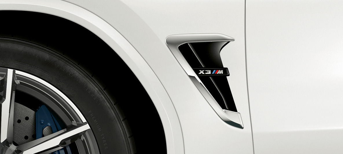 BMW X3 M, M štrbina. BMW X3 M vo farbe Alpine White, exteriér, M štrbiny s chrómovými prvkami a označením modelu.