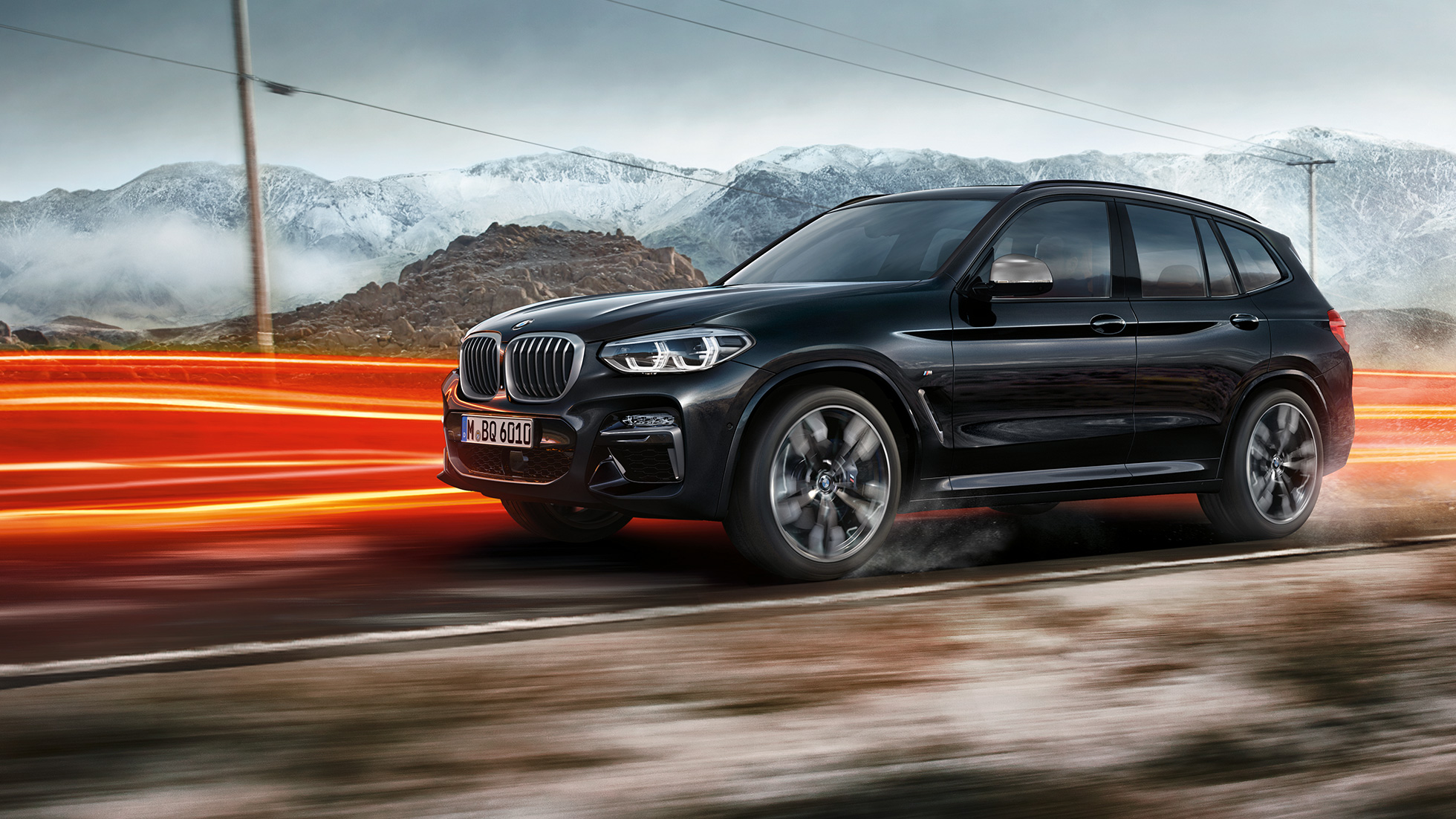 BMW X3 M40i a BMW X3 M40d, bočný pohľad. BMW X3 M40i a BMW X3 M40d v metalickej farbe Black Sapphire, jazda, exteriér, bočný pohľad pred horskou scenériou so svetelnými pásmi.