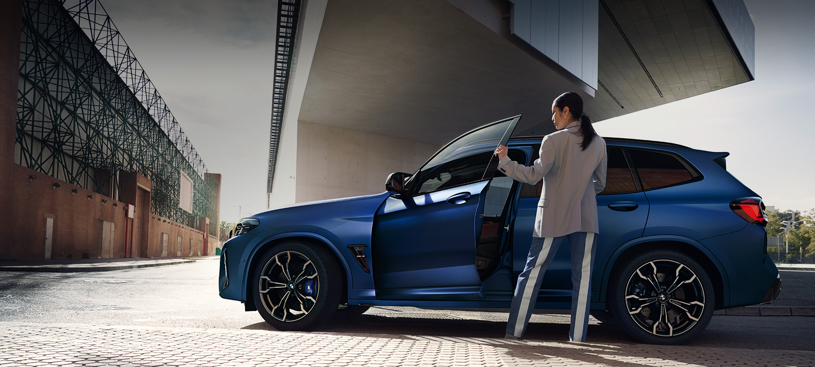 BMW X3 M Competition F97 LCI Facelift 2021 bočný pohľad statický BMW X3 M Competition F97 LCI Facelift 2021 BMW Individual metalíza Frozen Portimao Blue bočný pohľad statický s otvorenými dverami a modelkou