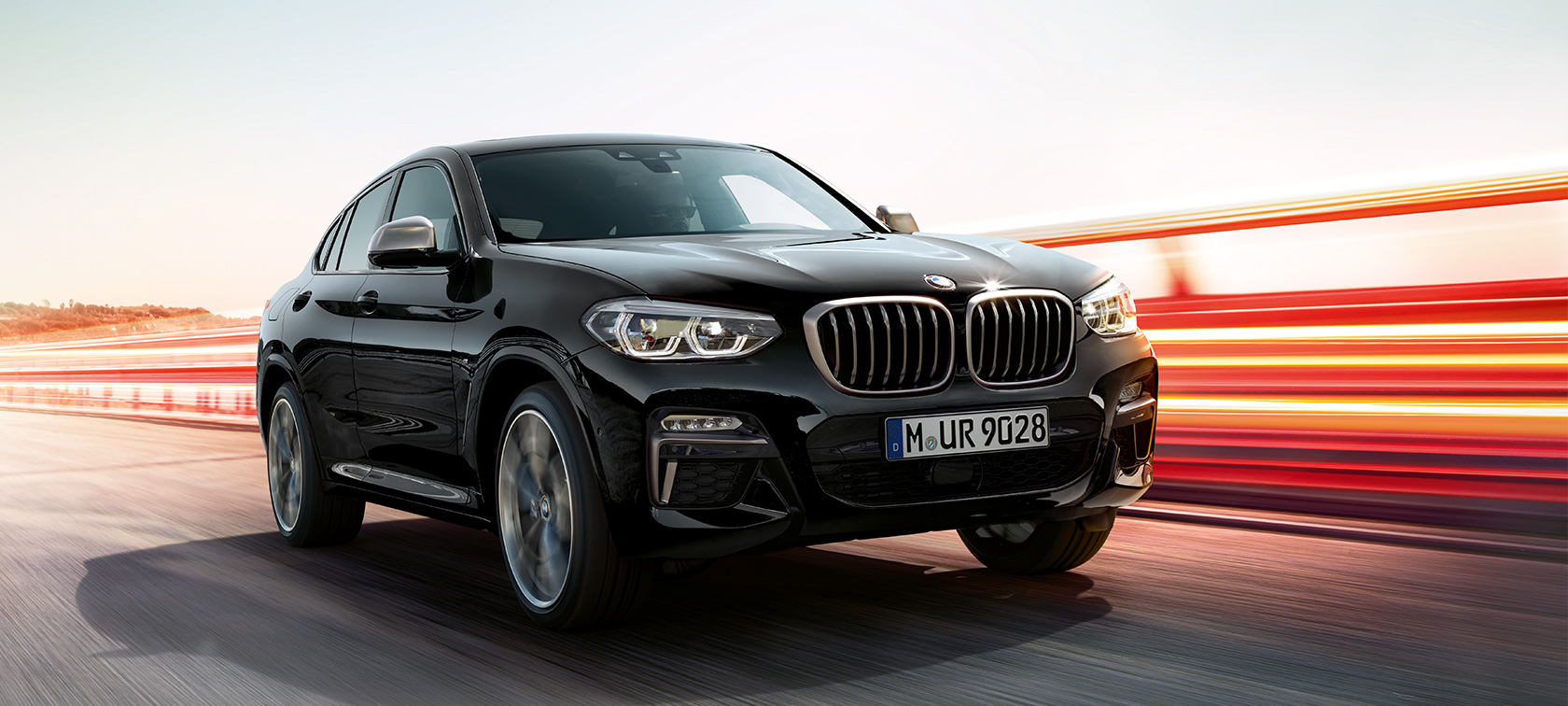 BMW X4 M40i a BMW X4 M40d, trojštvrťový predný pohľad, ľavá strana. BMW X4 M40i a BMW X4 M40d v metalickej farbe Black Sapphire, exteriér, trojštvrťový predný pohľad, ľavá strana so svetelnými pásmi.