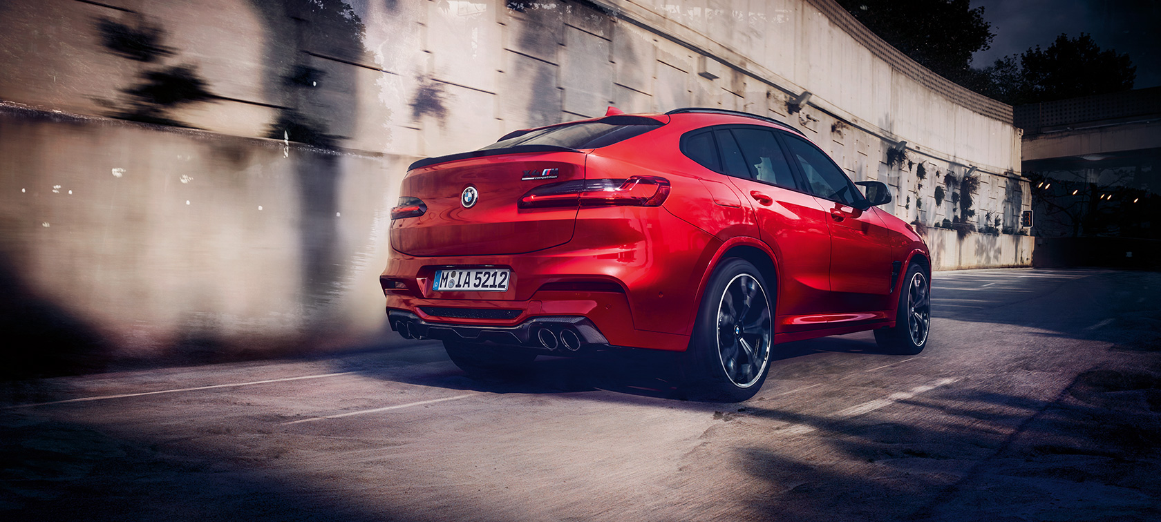 BMW X4 M Competition, trojštvrťový zadný pohľad. BMW X4 M Competition v metalickej farbe Toronto Red, jazda, exteriér, trojštvrťový zadný pohľad.